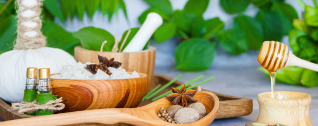 Cinnamon, dry ginger, black cardamom, javitri, long pepper and green leaves in mortar and pestle and scattered ayurvedic pills on white background